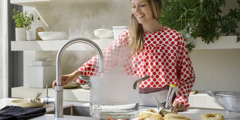 Junge Familienfrau bedient einen dampfenden Quooker.